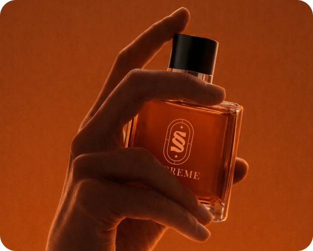 Hand holding Supreme amber perfume bottle against warm orange background