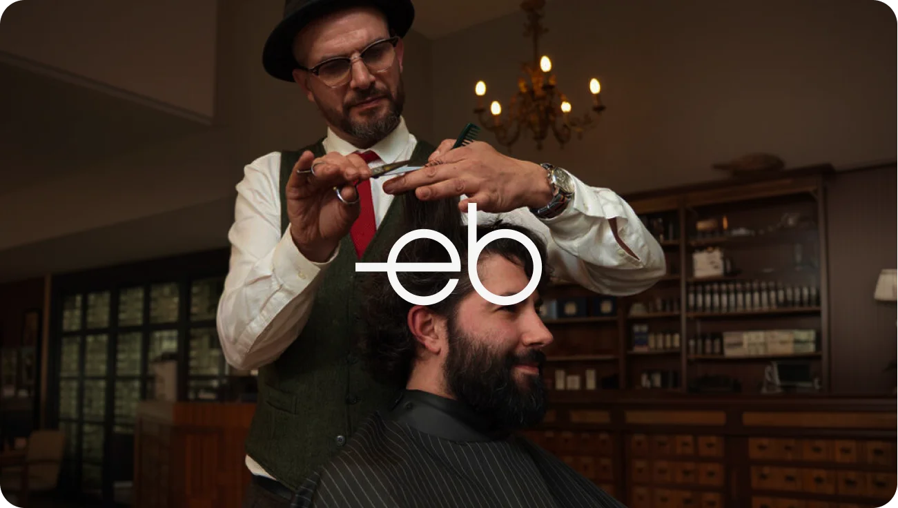 Professional barber trimming client hair with EB logo overlay in classic barbershop